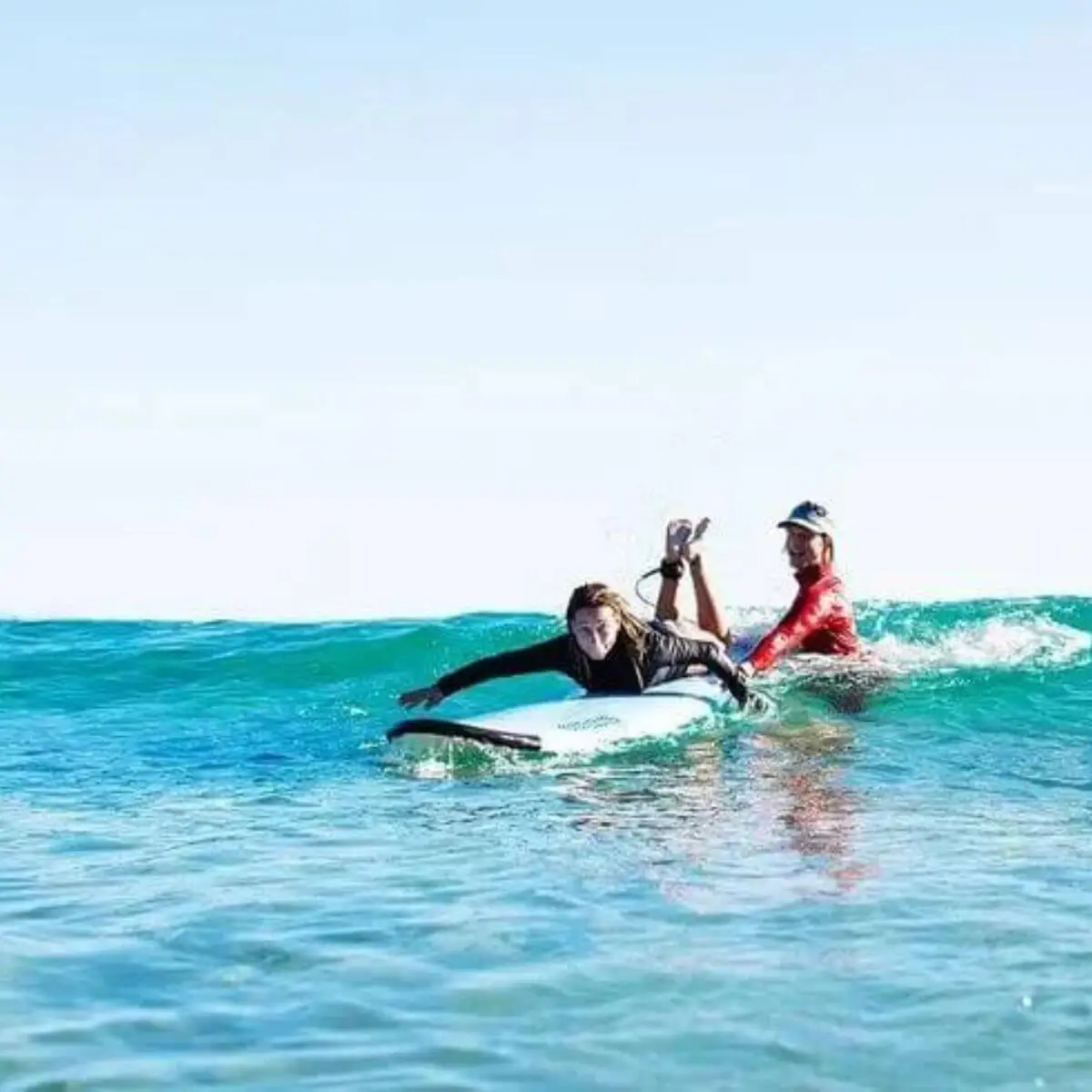 A surfing instructor pushing a stuedent to  a wave 