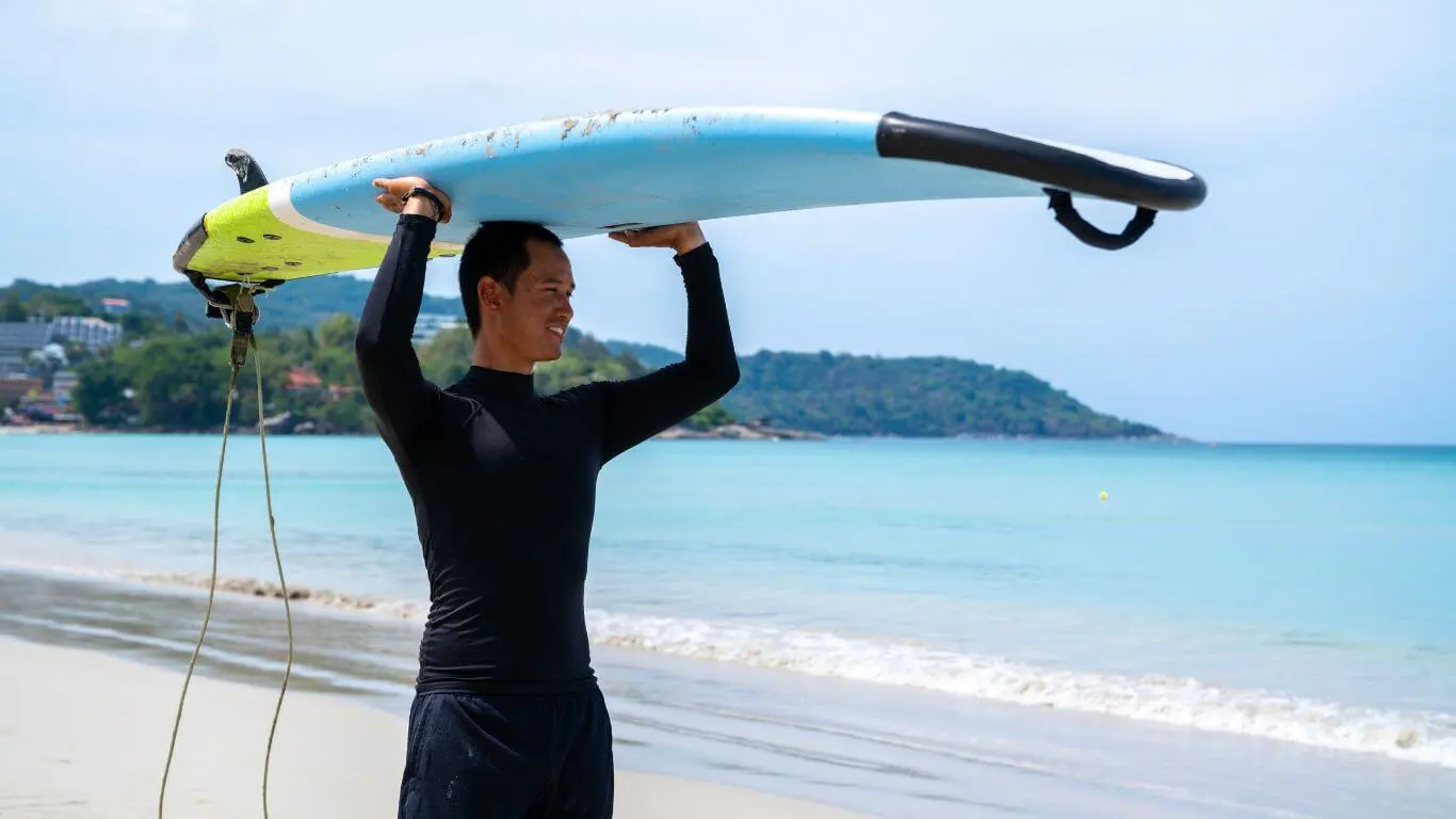 a surfer wearing a rash guard and carrying a surfboard on his head